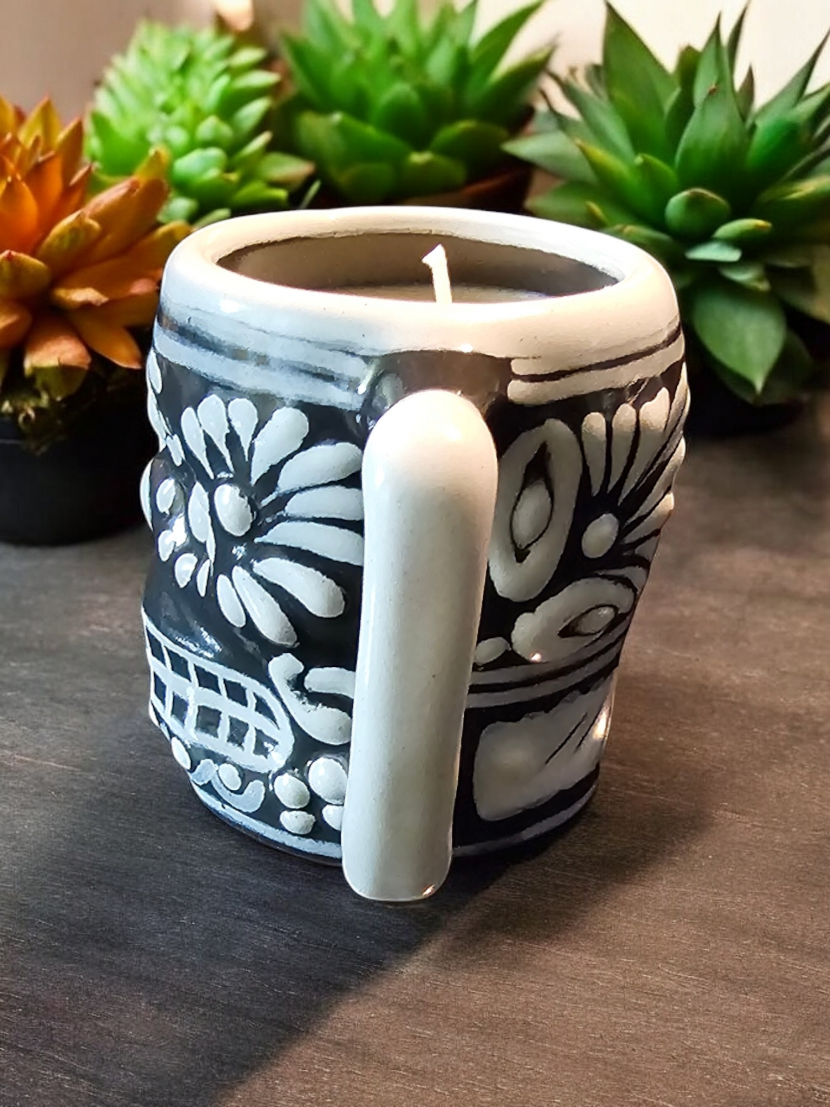 The Vela Lady Calavera shot glass candle with white floral designs on a black Talavera ceramic vessel.
