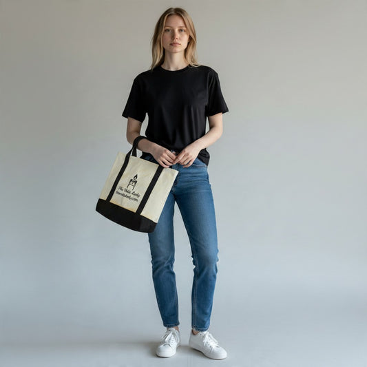 A woman holding The Vela Lady natural canvas tote bag with black accents and branding against a neutral background.