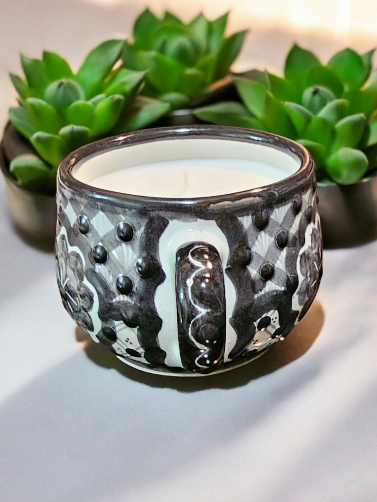 The Vela Lady La Catrina Talavera mug candle with black and white hand-painted patterns and soy wax in a succulent setting