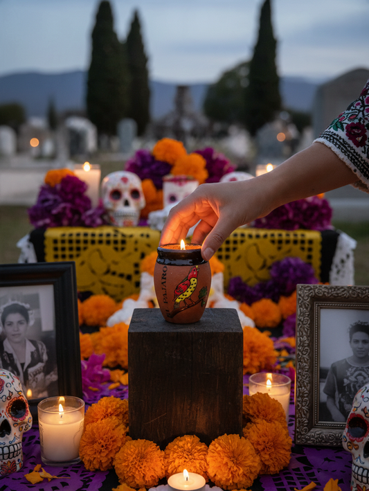 The Vela Lady El Pajaro Cantarito soy candle on a traditional Dia de los Muertos altar with marigolds and sugar skulls.