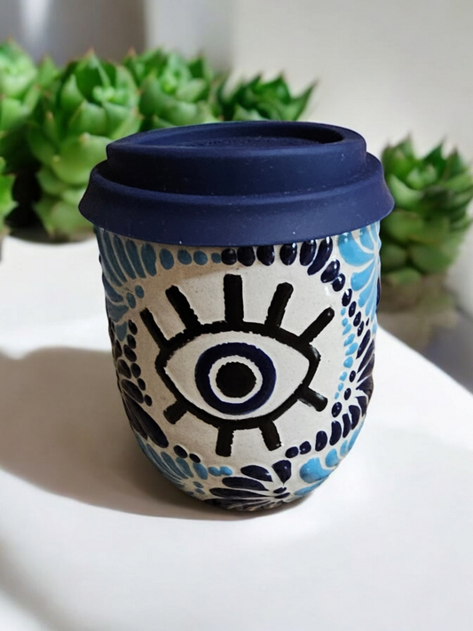 The Vela Lady Buenas Vibras Evil Eye Talavera tumbler candle with a blue lid and hand-painted Mexican ceramic design.