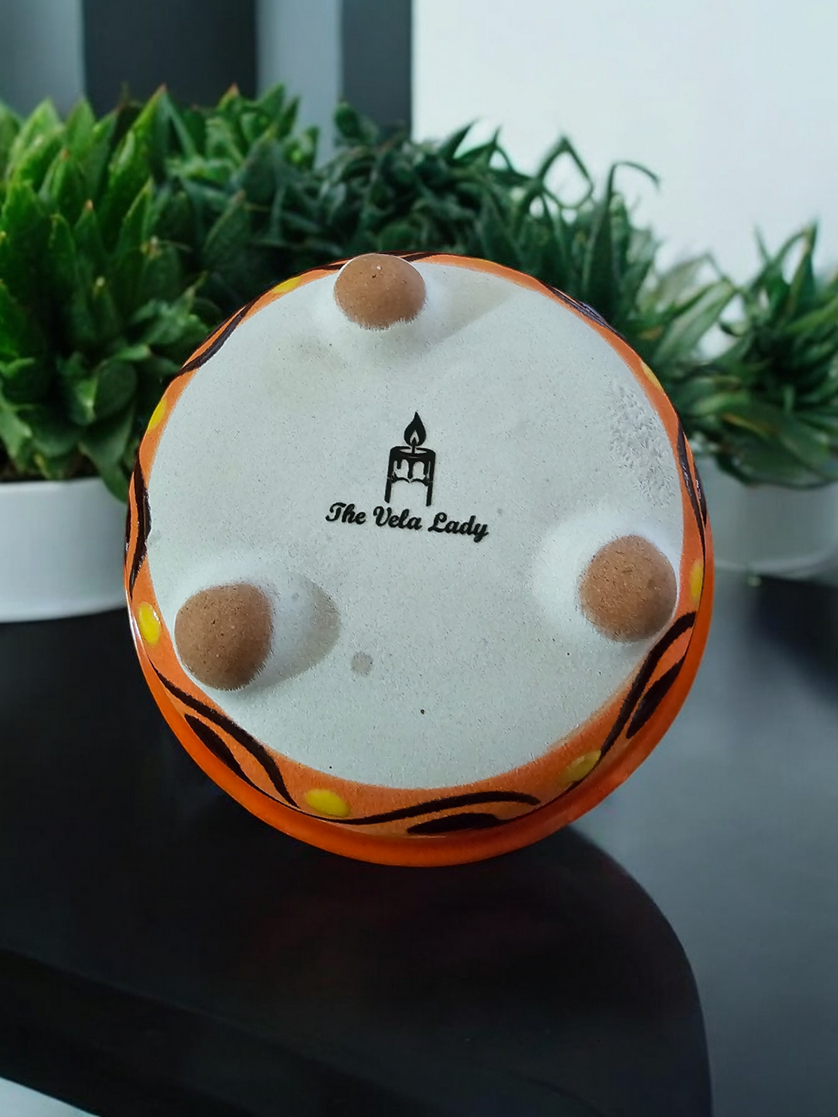 The Vela Lady handmade orange and light brown Mexican barro pottery candle bowl showing the branded base with feet.
