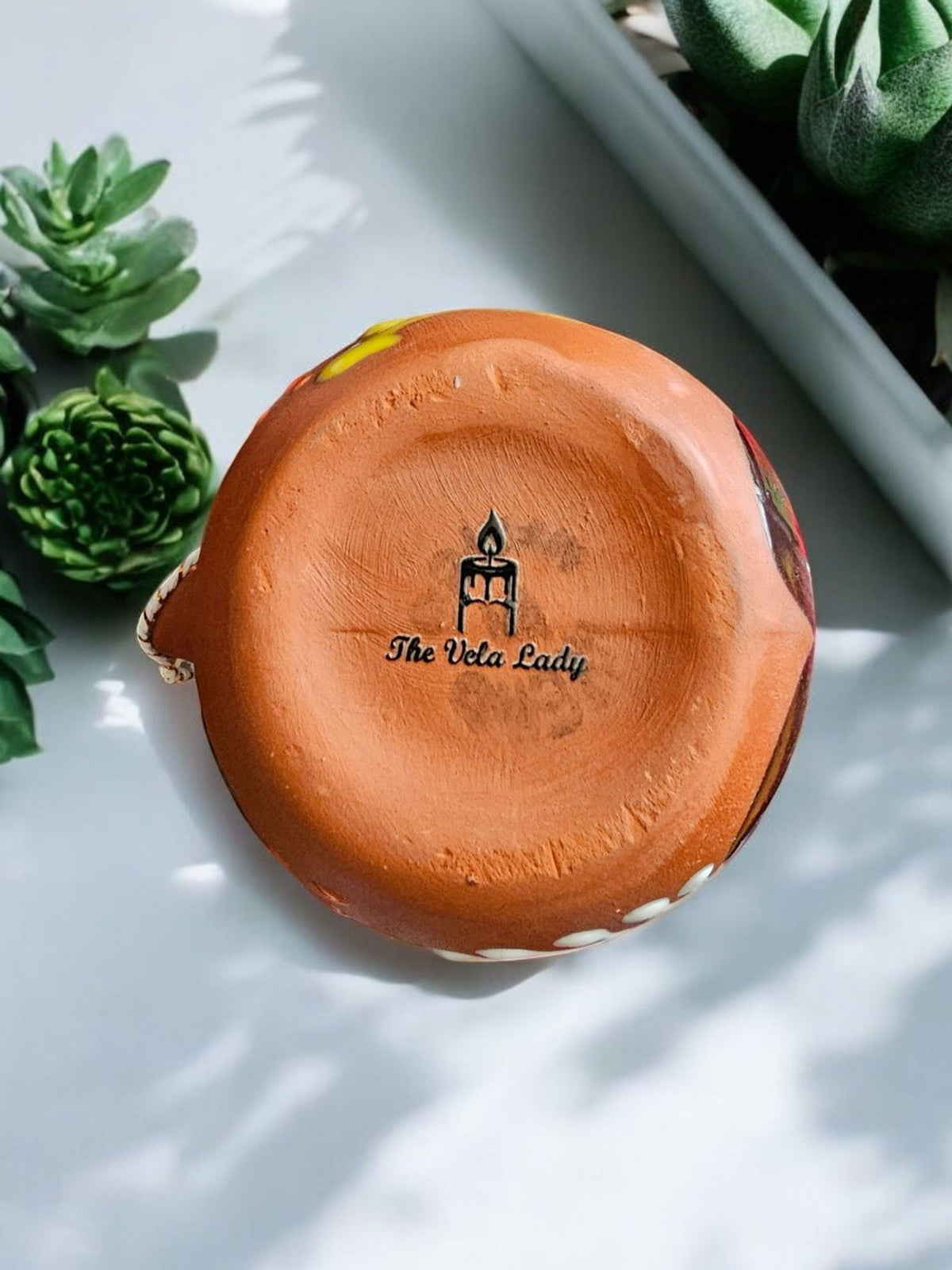 Bottom view of The Vela Lady handmade Mexican barro clay taza mug candle showing the brand logo stamp