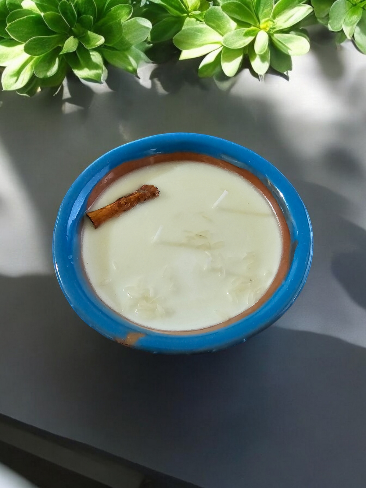 The Vela Lady light blue handmade barro salsa bowl soy candle topped with a cinnamon stick and rice grains