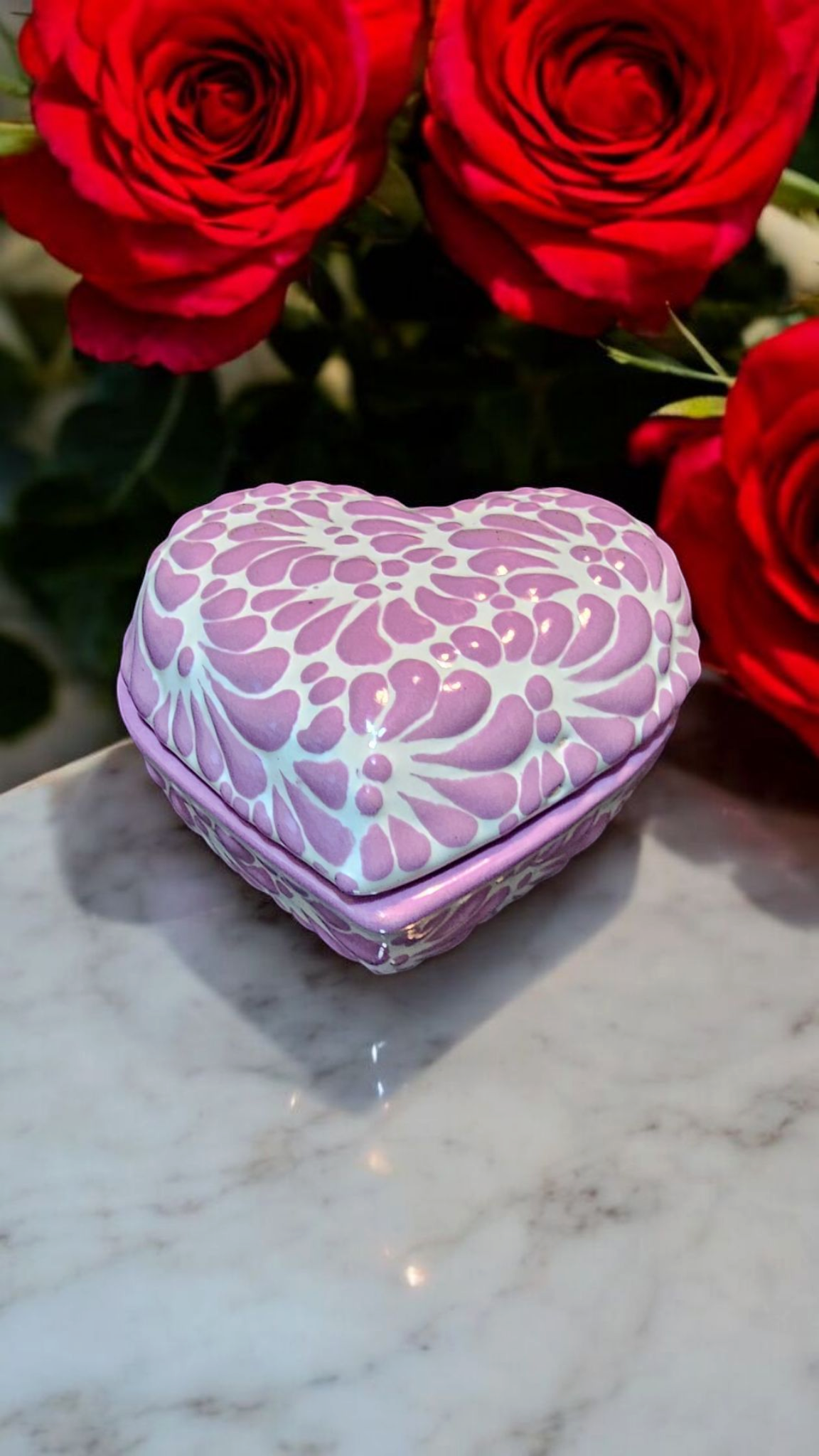 The Vela Lady heart-shaped purple and white Talavera ceramic trinket holder with floral pattern near red roses.