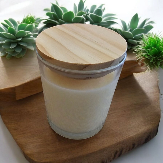 The Vela Lady soy wax candle in a glass jar with a wooden lid, displayed on a wooden board with succulent plants.