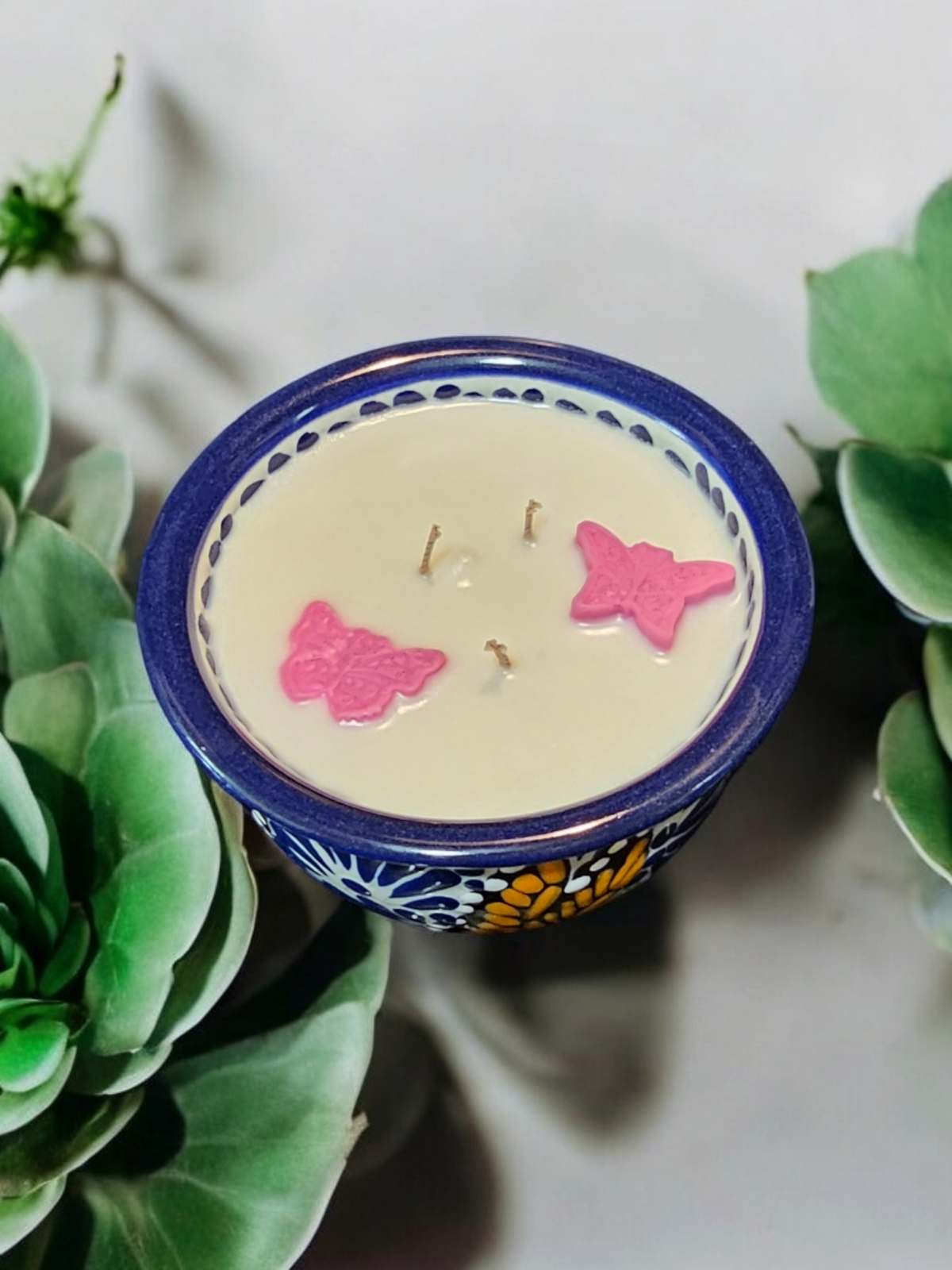 The Vela Lady blue and white Talavera barro salsa bowl soy candle featuring pink butterfly wax embeds and three wicks.