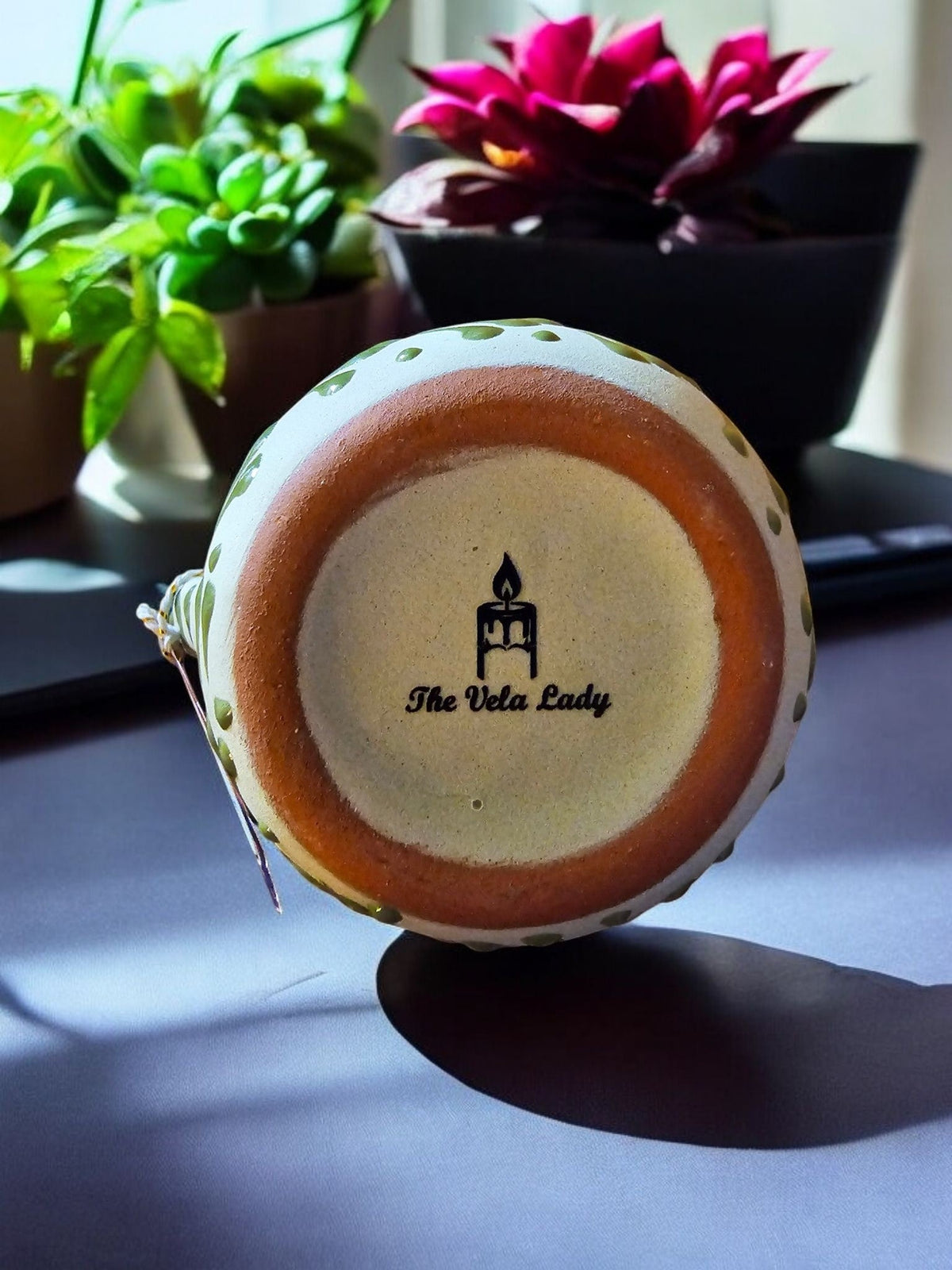 The Vela Lady Mangoneada scented candle in a handmade yellow Mexican barro mug with brand logo on the base.