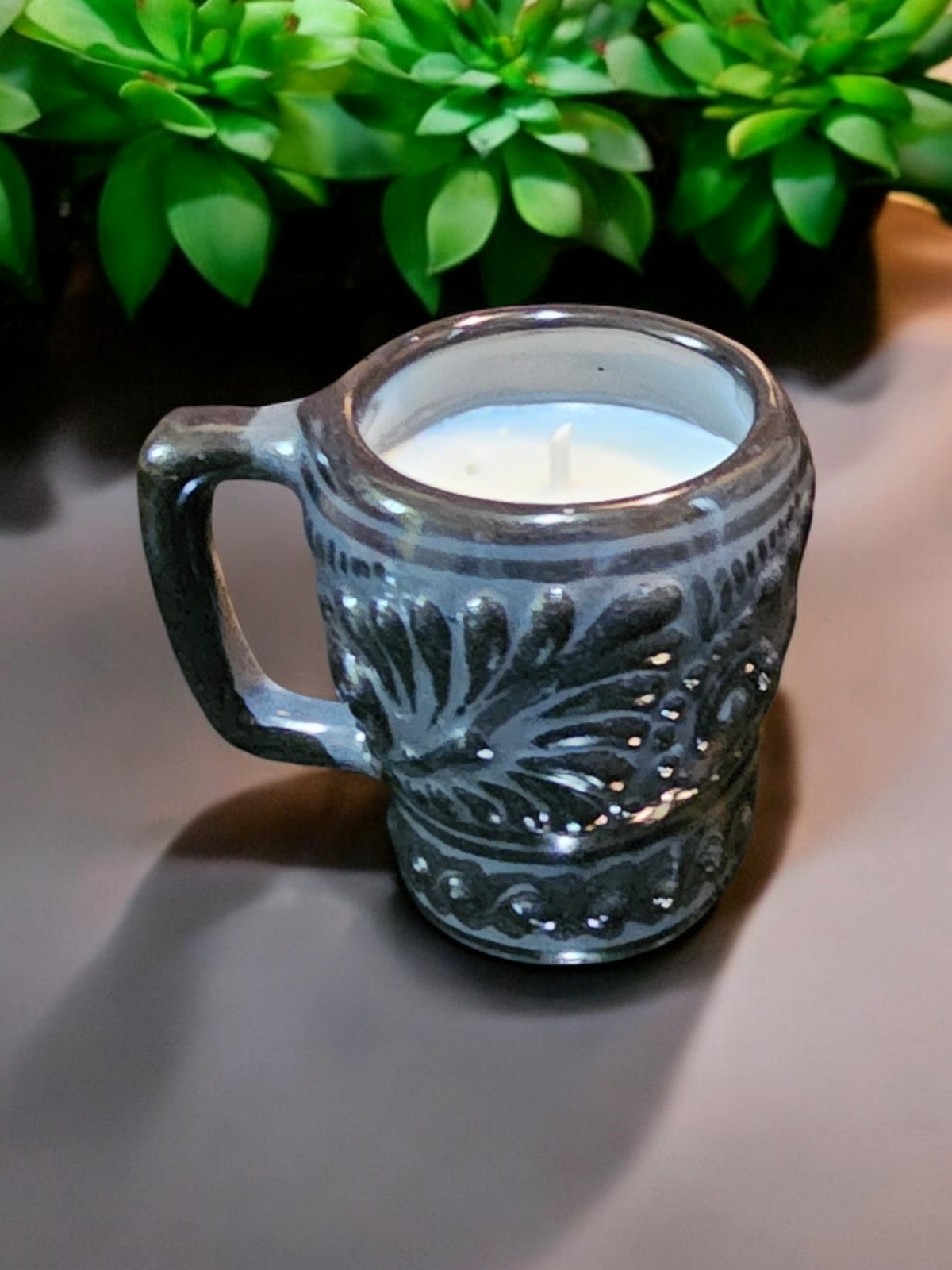 The Vela Lady black Talavera shot glass candle with soy wax, featuring intricate embossed floral patterns.