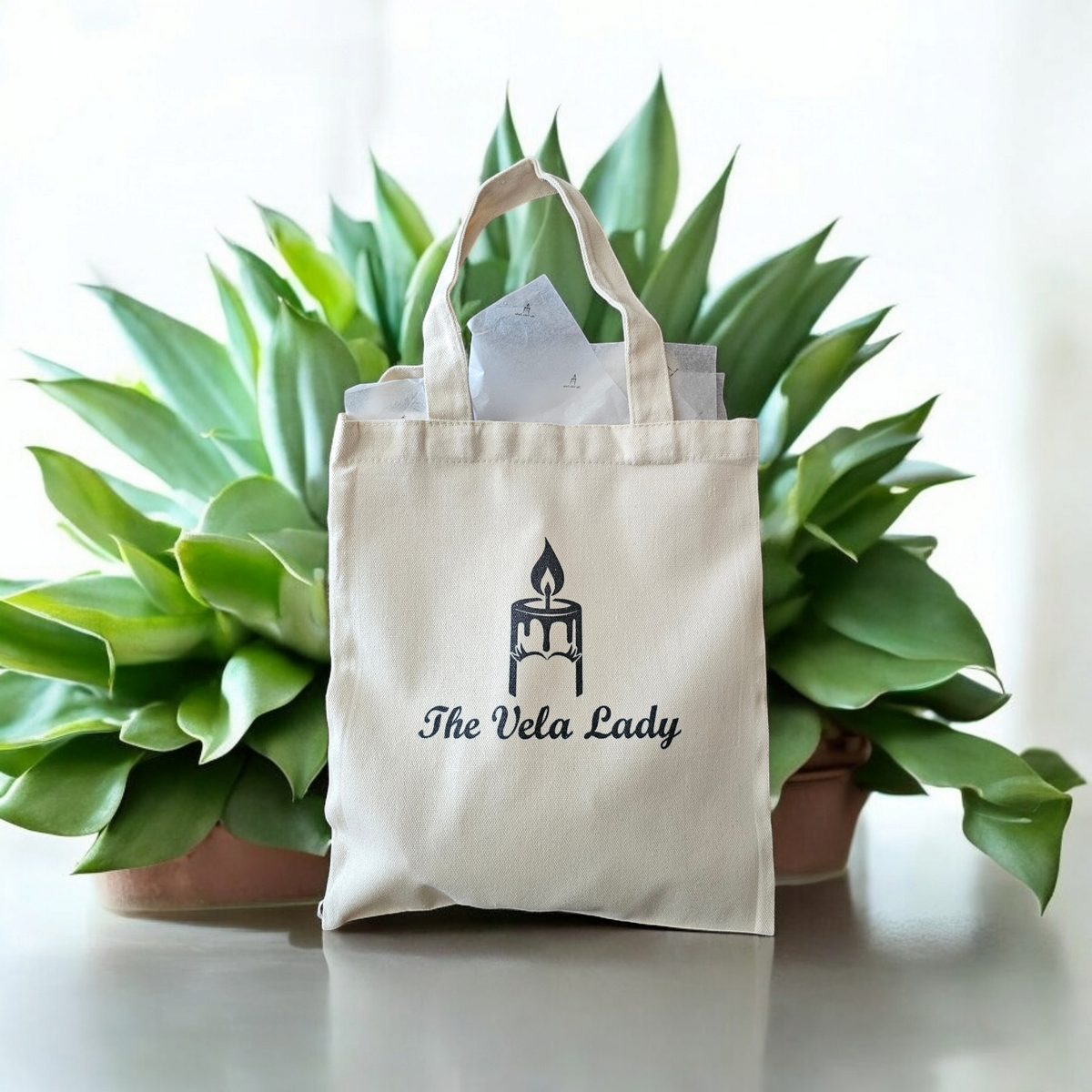 The Vela Lady natural cotton canvas gift tote bag with candle logo, featuring sturdy handles and tissue paper.