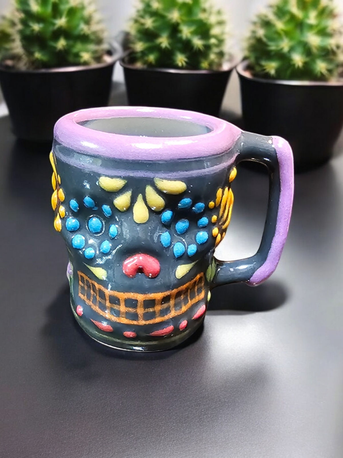The Vela Lady Calavera shot glass candle featuring a grey skull design with colorful hand-painted details.