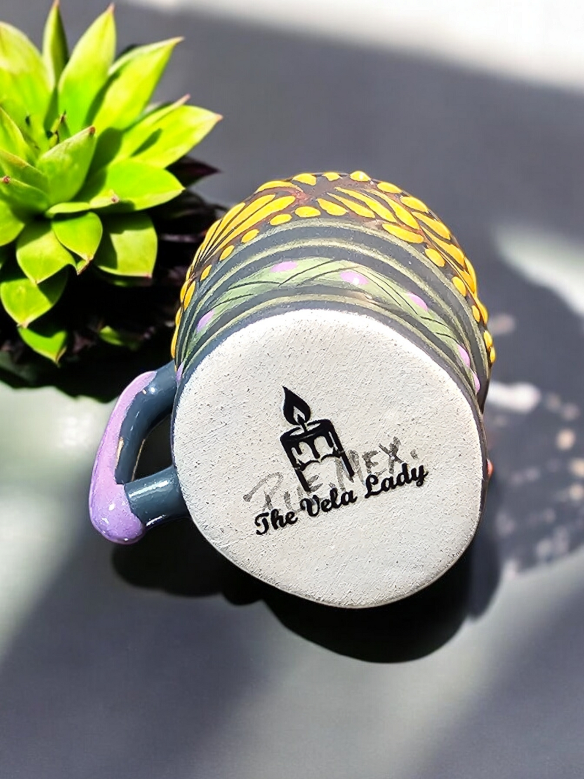 The Vela Lady handmade Talavera shot glass candle with a blue and yellow calavera design, viewed from the bottom.
