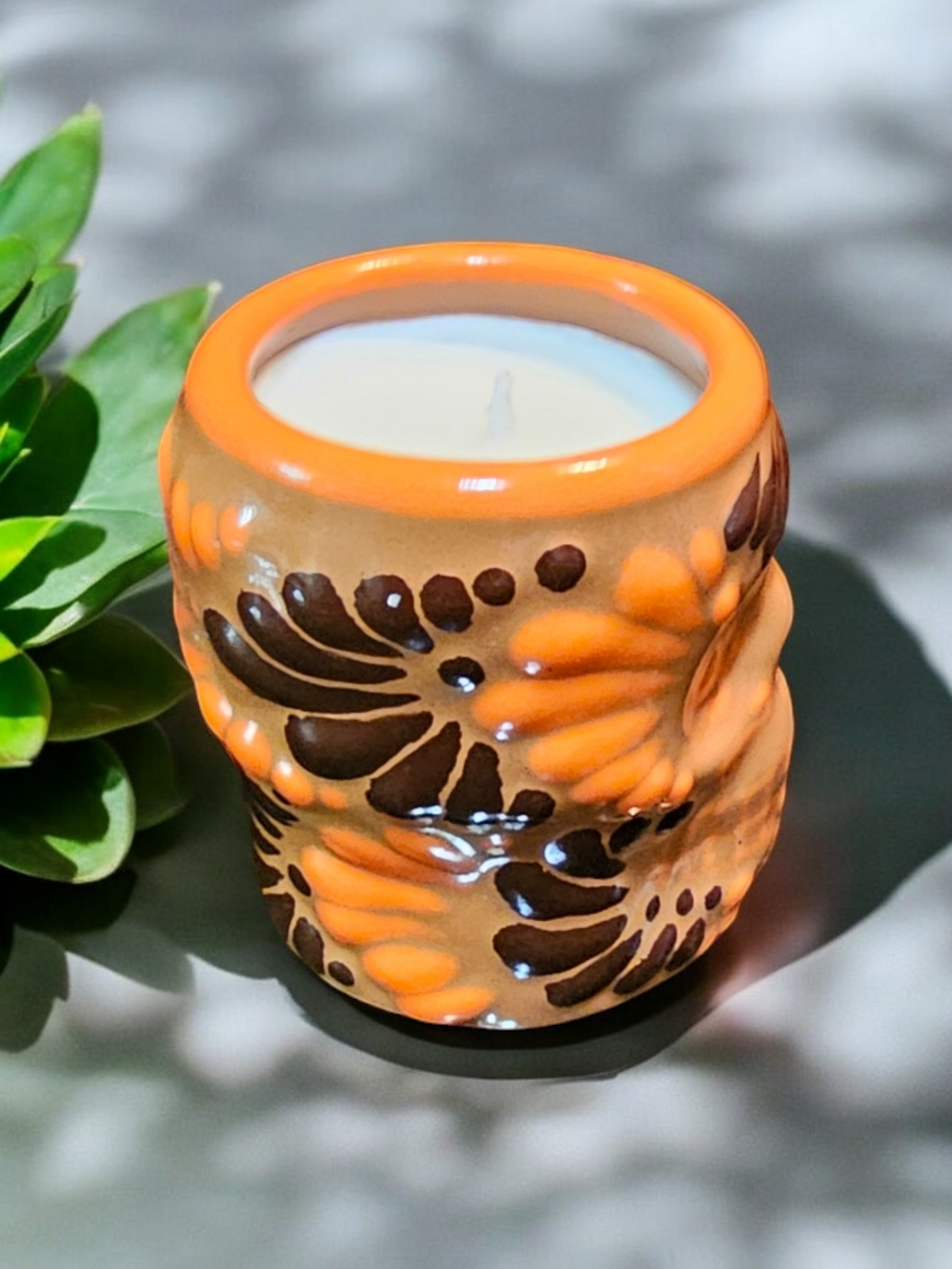 The Vela Lady Calavera shot glass candle in orange and brown hand-painted Mexican Talavera ceramic with soy wax.