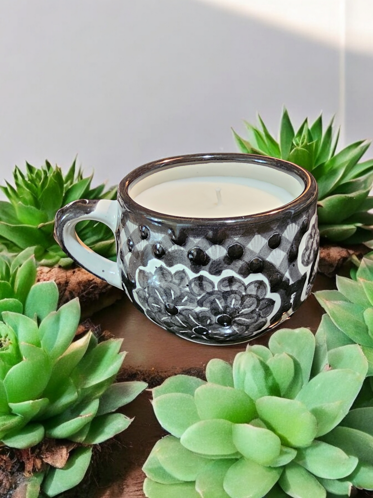 The Vela Lady La Catrina Talavera mug candle in black and white floral pattern surrounded by green succulent plants