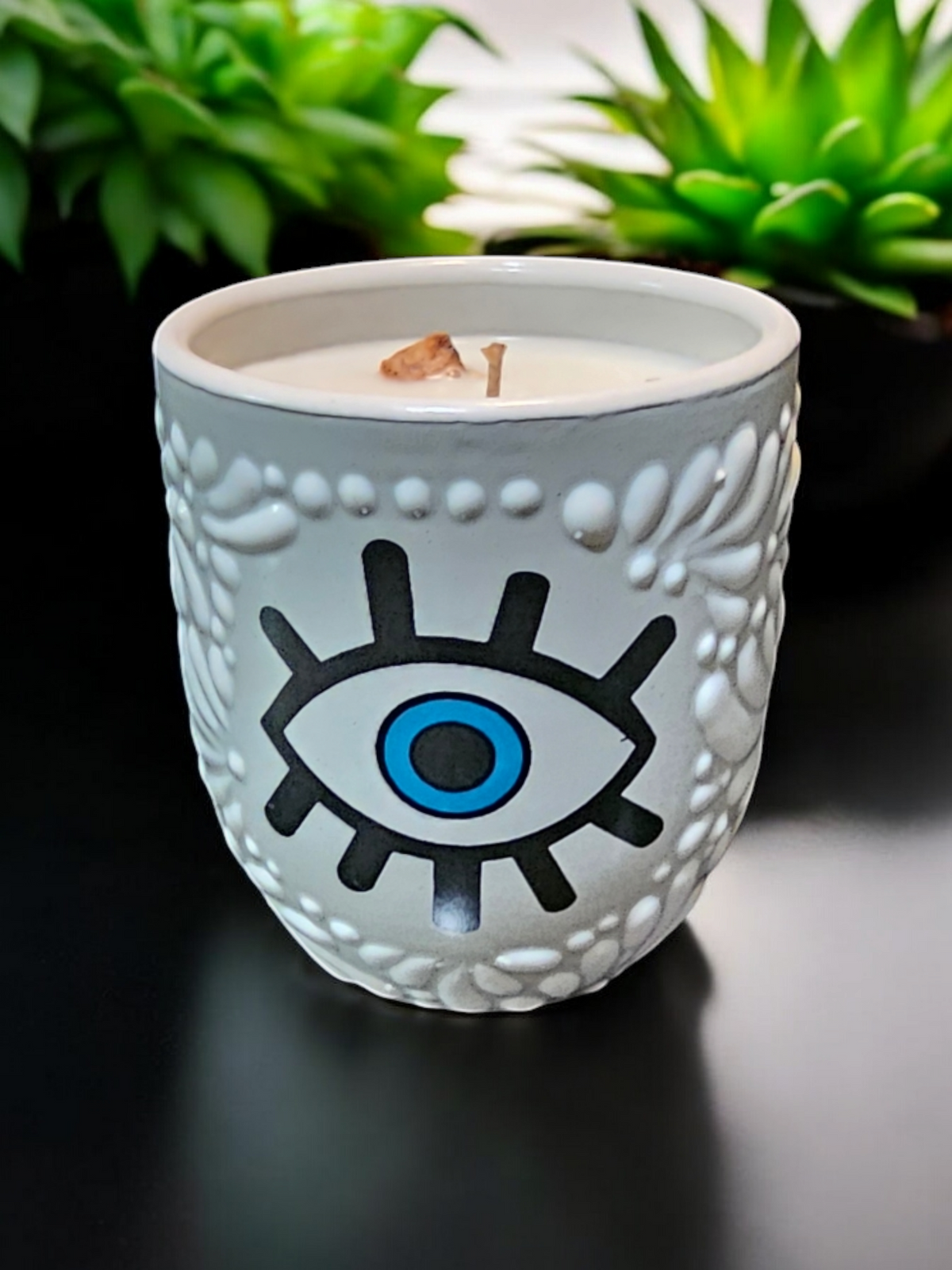 The Vela Lady Buenas Vibras soy wax candle in a white handcrafted Mexican Talavera barro tumbler with an evil eye design.