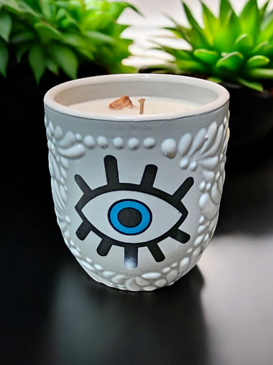 The Vela Lady Buenas Vibras soy wax candle in a white handcrafted Mexican Talavera barro tumbler with an evil eye design.