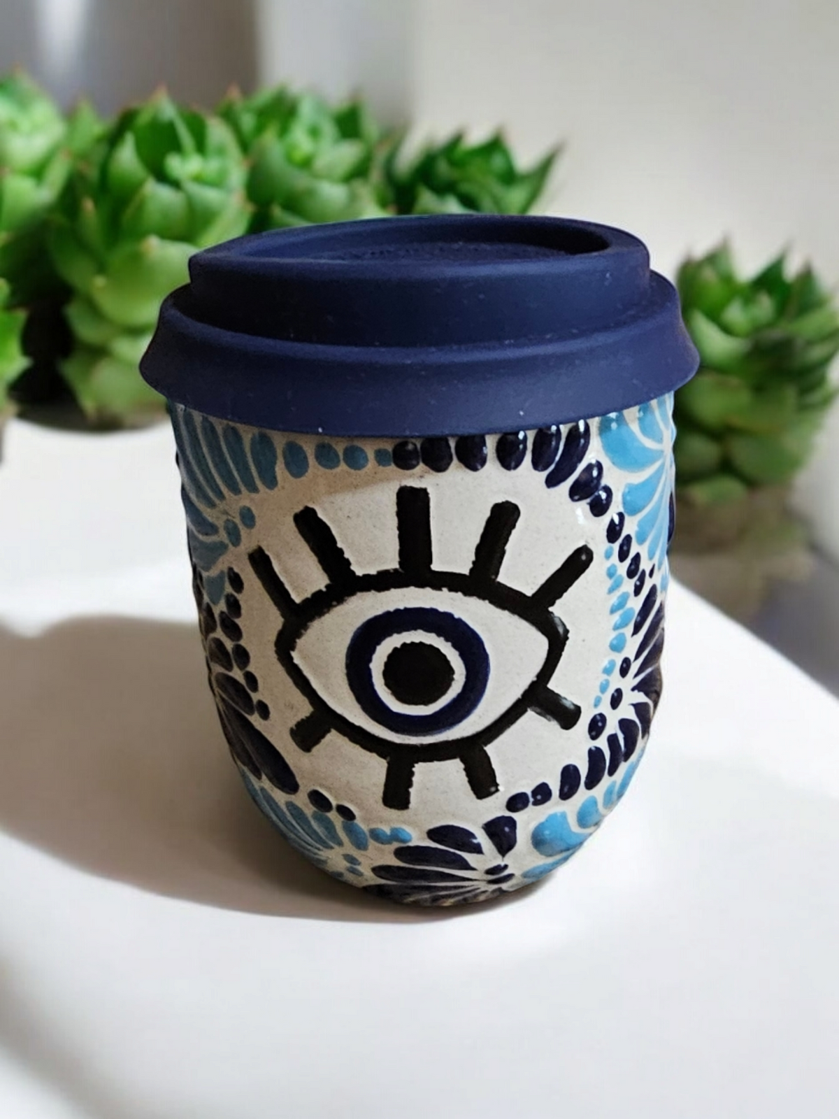 The Vela Lady Buenas Vibras Evil Eye Talavera tumbler candle with a blue lid and hand-painted Mexican ceramic design.