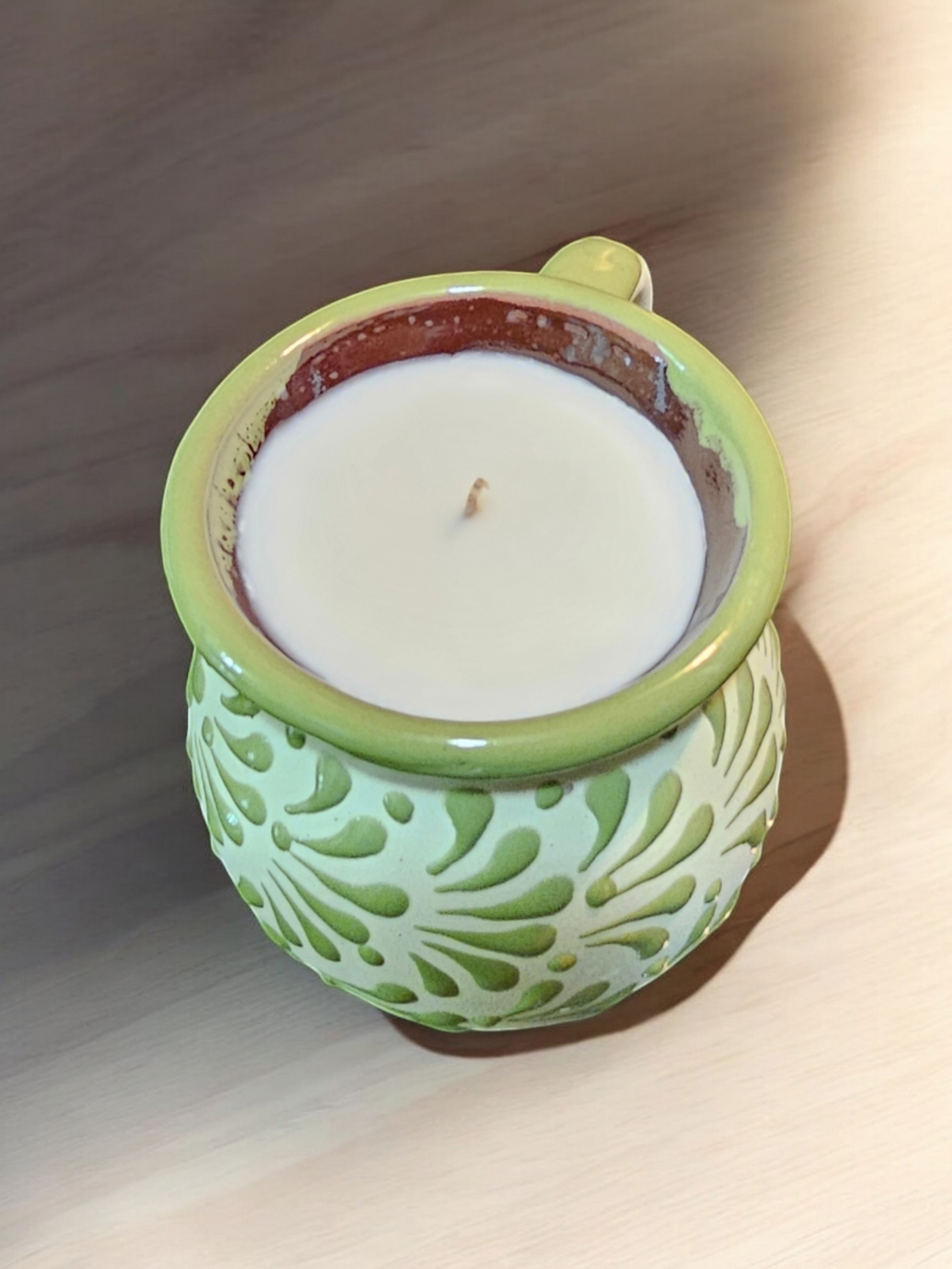 The Vela Lady green handmade Mexican barro mug candle with soy wax and agua fresca scent on a wooden surface