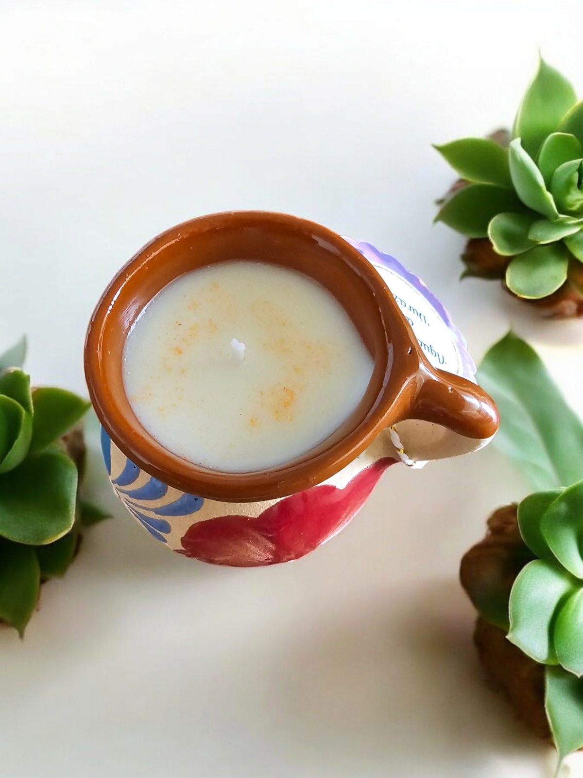 The Vela Lady handmade Mexican barro tazita shot mug candle with soy wax, featuring colorful hand-painted floral art.