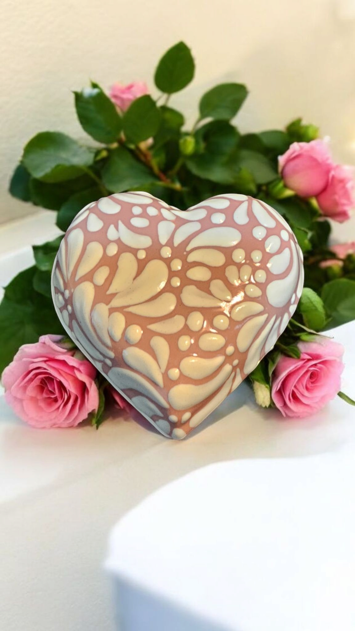 The Vela Lady heart-shaped Talavera trinket holder with white floral patterns on a pink background, set with roses.