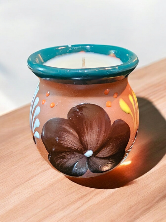The Vela Lady handmade Mexican barro mug candle with dark floral hand-painted design and teal rim on wooden surface