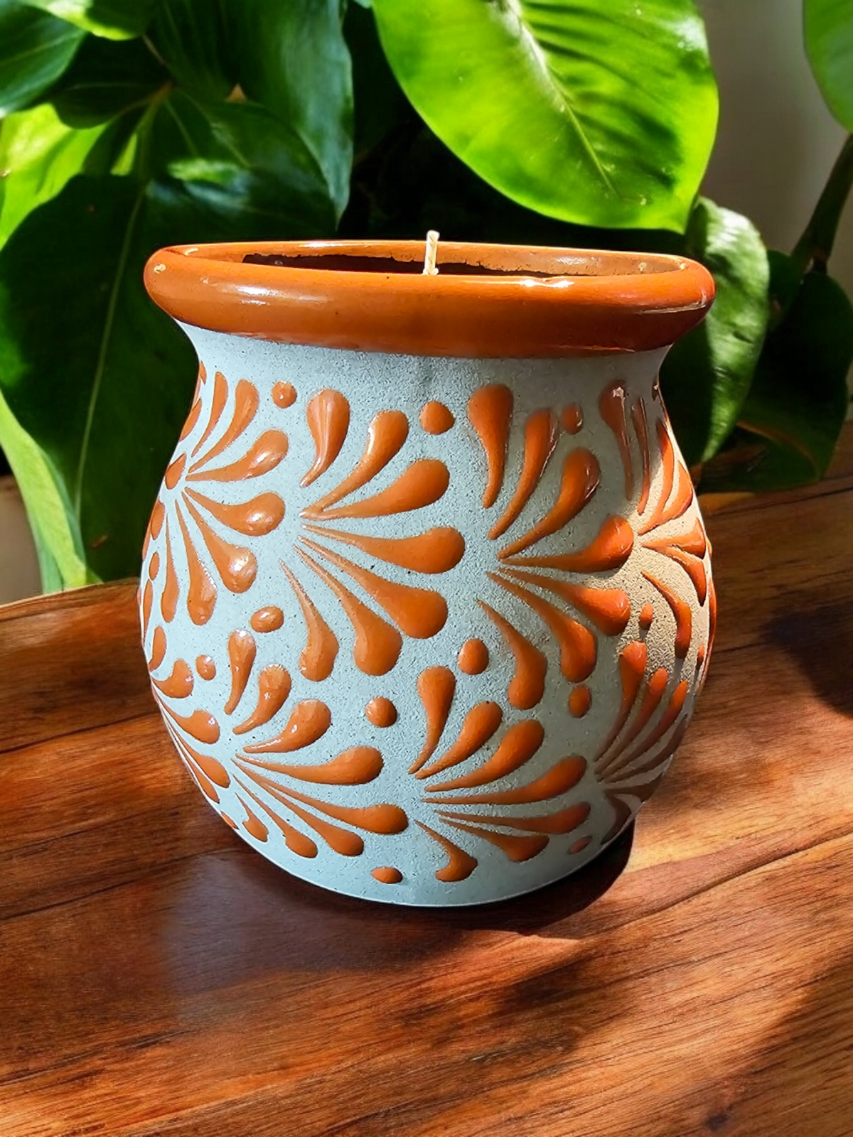 The Vela Lady orange and cream hand-painted Mexican barro mug candle with intricate floral patterns on a wooden table.