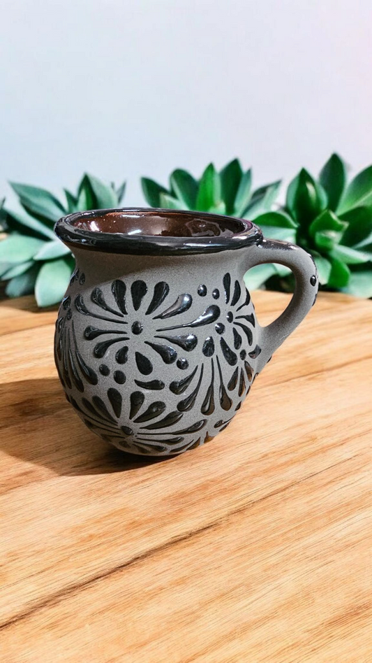 The Vela Lady Papacito Collection handmade gray Mexican barro mug with black floral patterns on a wooden surface.