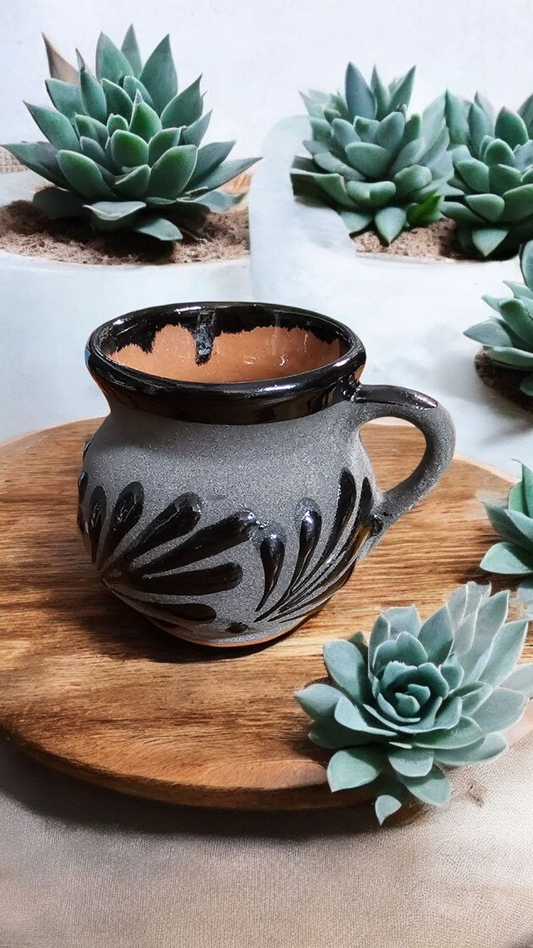 The Vela Lady Papacito Collection handmade Mexican barro tazita candle in black on gray with hand-painted details.