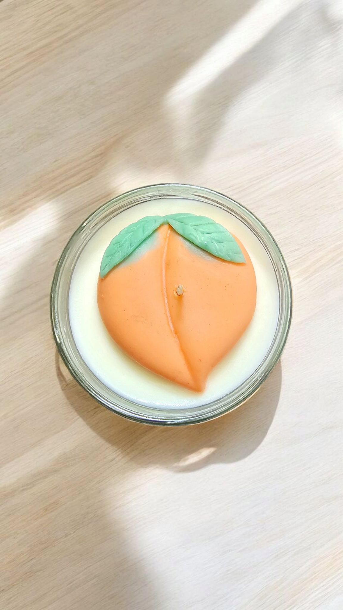 The Vela Lady soy wax candle in a glass jar featuring a decorative peach-shaped wax topper with green leaves