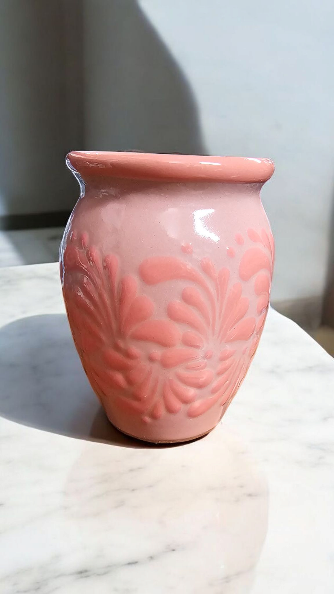 The Vela Lady pink handmade Mexican lead free barro cantarito premium soy wax candle made with clean frgrance oils with embossed floral patterns on a marble surface.