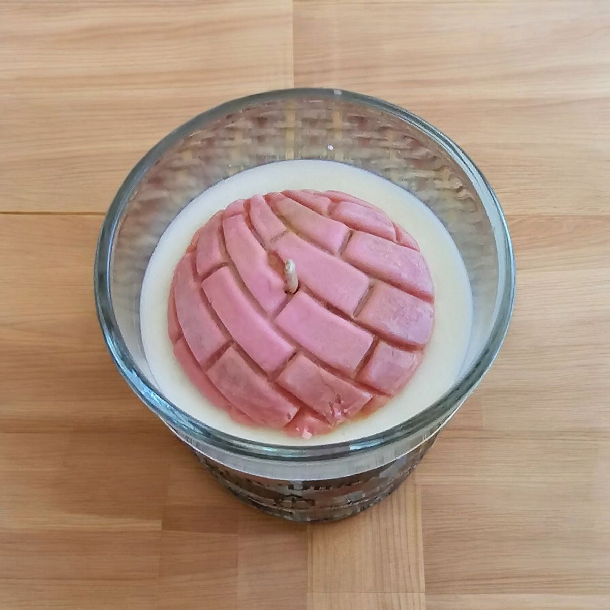The Vela Lady soy wax candle in a glass jar featuring a pink concha bread shaped wax topper on a wooden surface