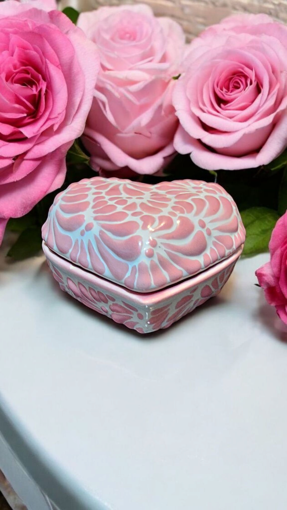 The Vela Lady heart-shaped pink and white Talavera ceramic trinket holder surrounded by fresh pink roses.