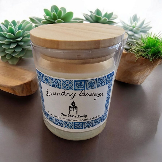 The Vela Lady Laundry Breeze soy wax candle in a glass jar with a wooden lid, surrounded by decorative succulents.