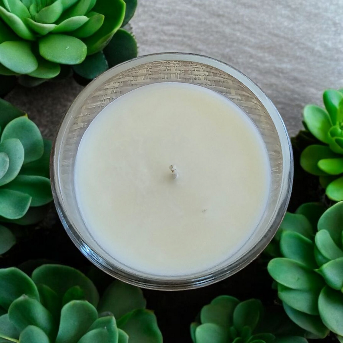 Top view of a The Vela Lady soy wax candle in a glass jar surrounded by green succulent plants.