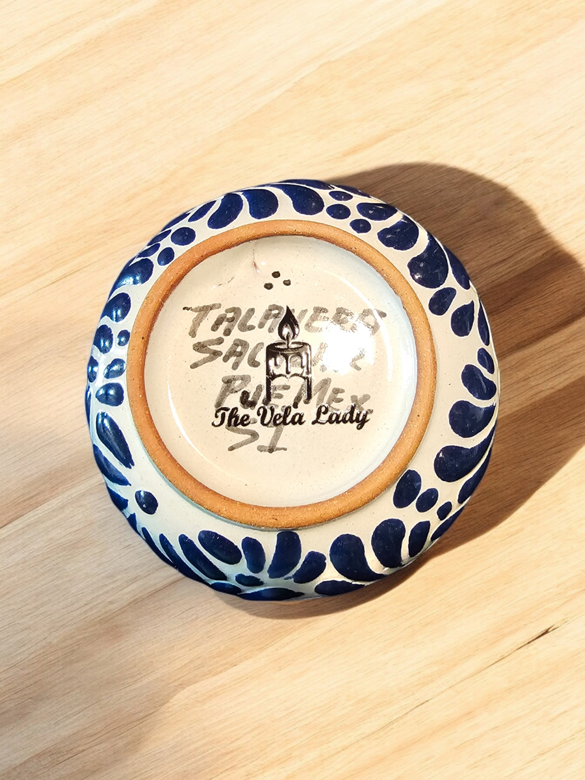 The Vela Lady blue and white Talavera ceramic candle vessel base with artisan signature on a wooden surface.