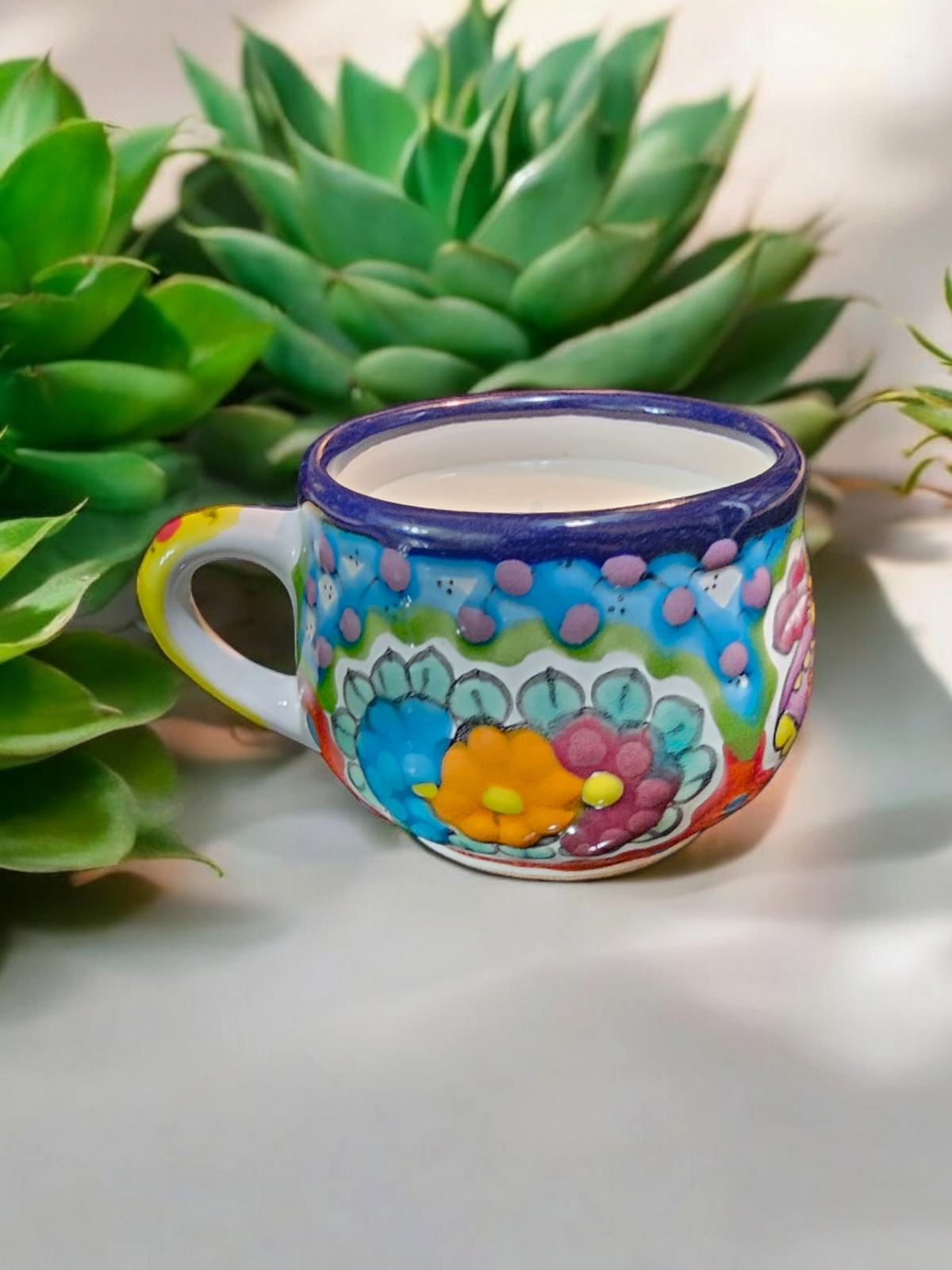 The Vela Lady La Catrina Talavera mug candle with vibrant hand-painted floral patterns and soy wax in a green setting