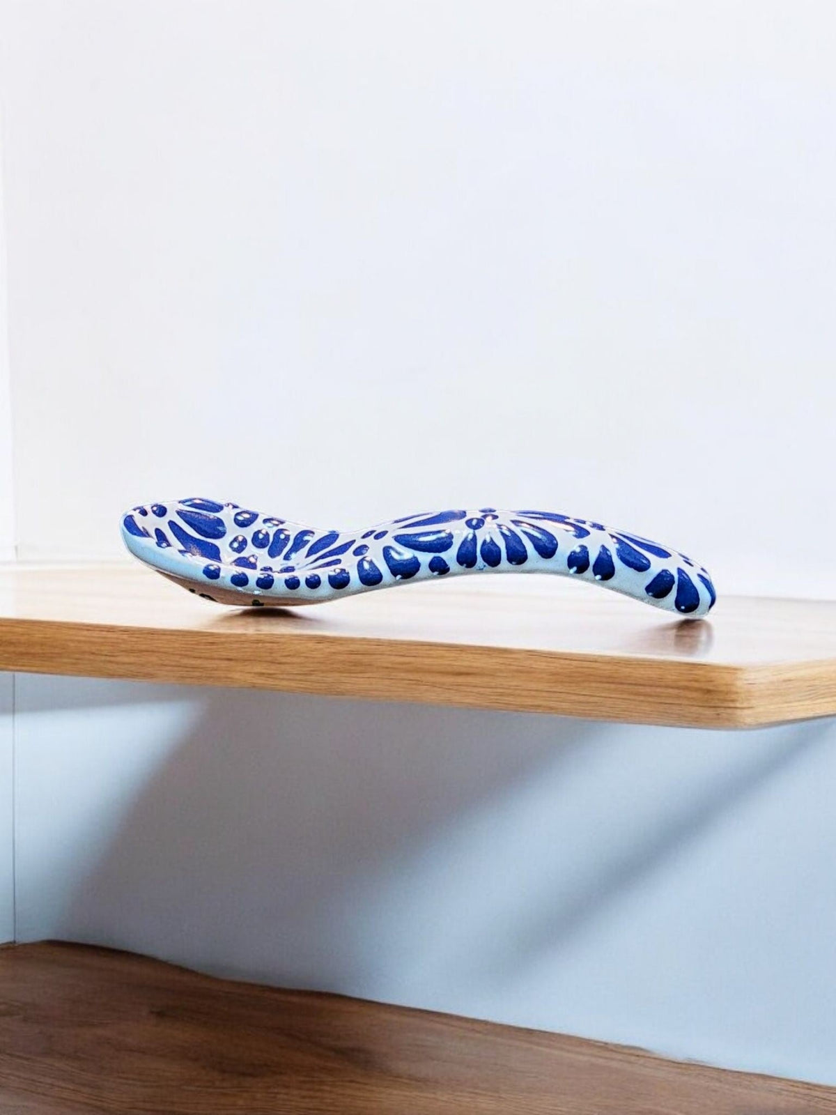 The Vela Lady handcrafted blue and white Talavera barro ceramic spoon with intricate floral patterns on a wooden shelf.
