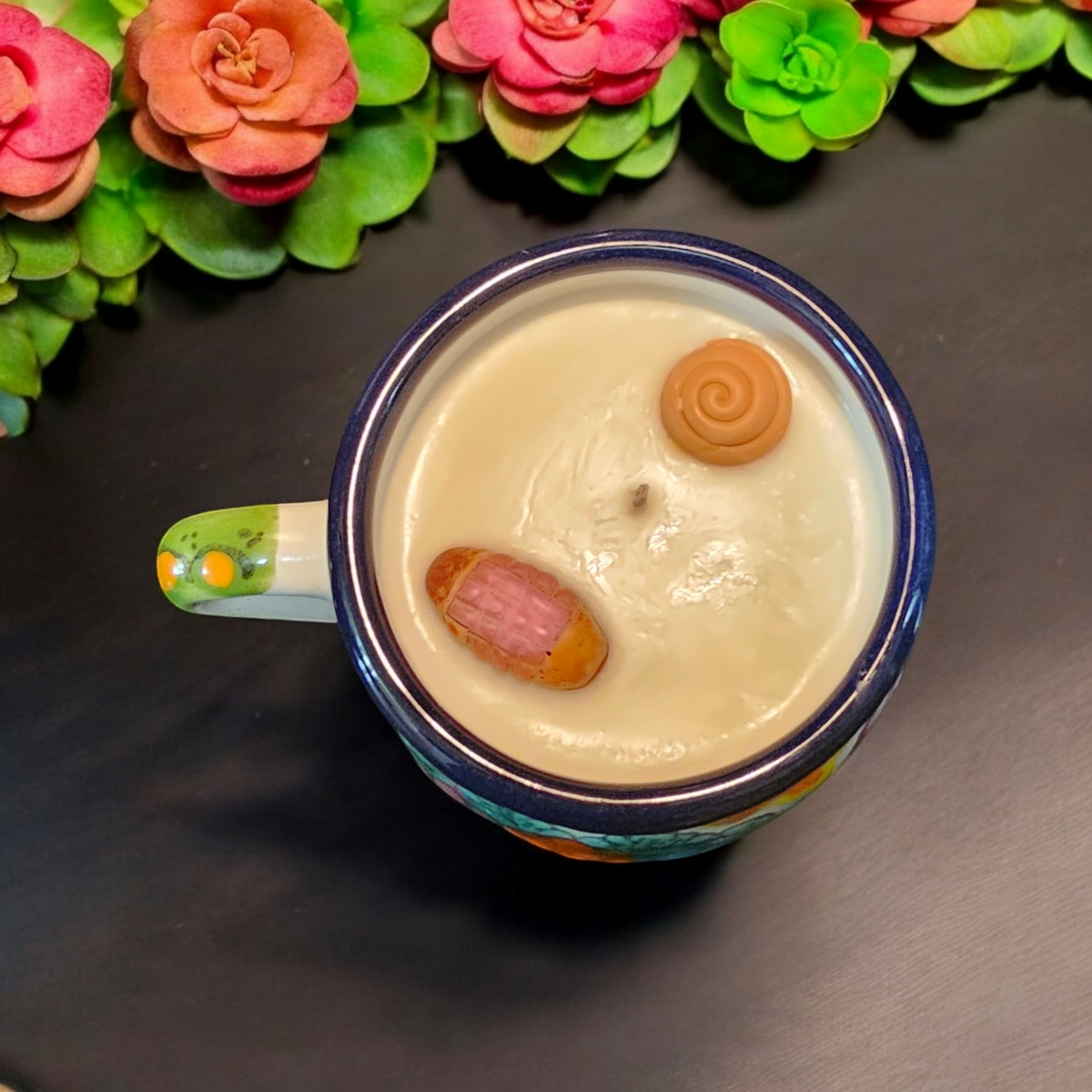 The Vela Lady La Catrina Talavera mug candle with soy wax and decorative wax toppings on a black surface