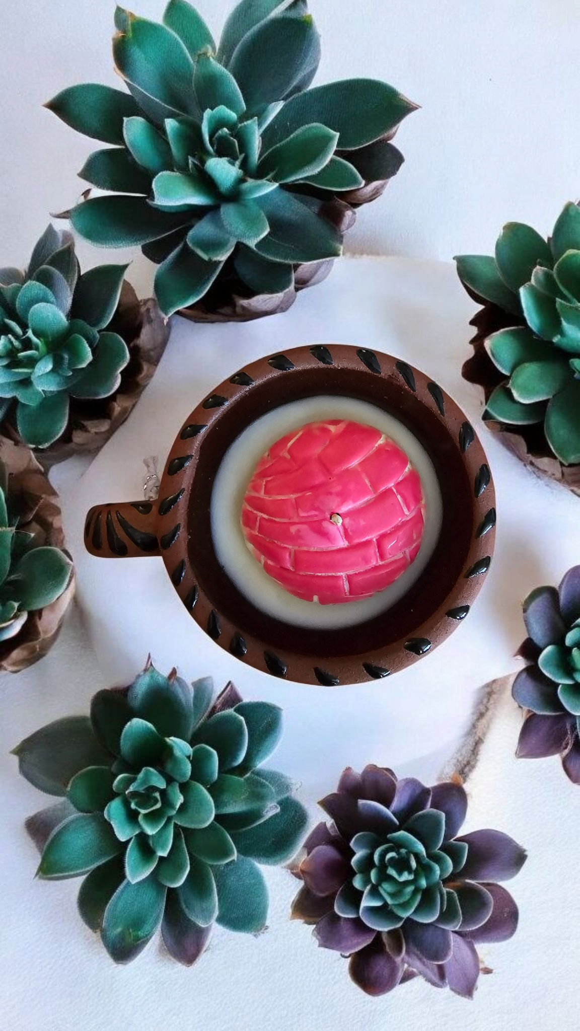 The Vela Lady Taza Collection candle in a dark handmade Mexican barro mug with a pink concha-shaped soy wax top.