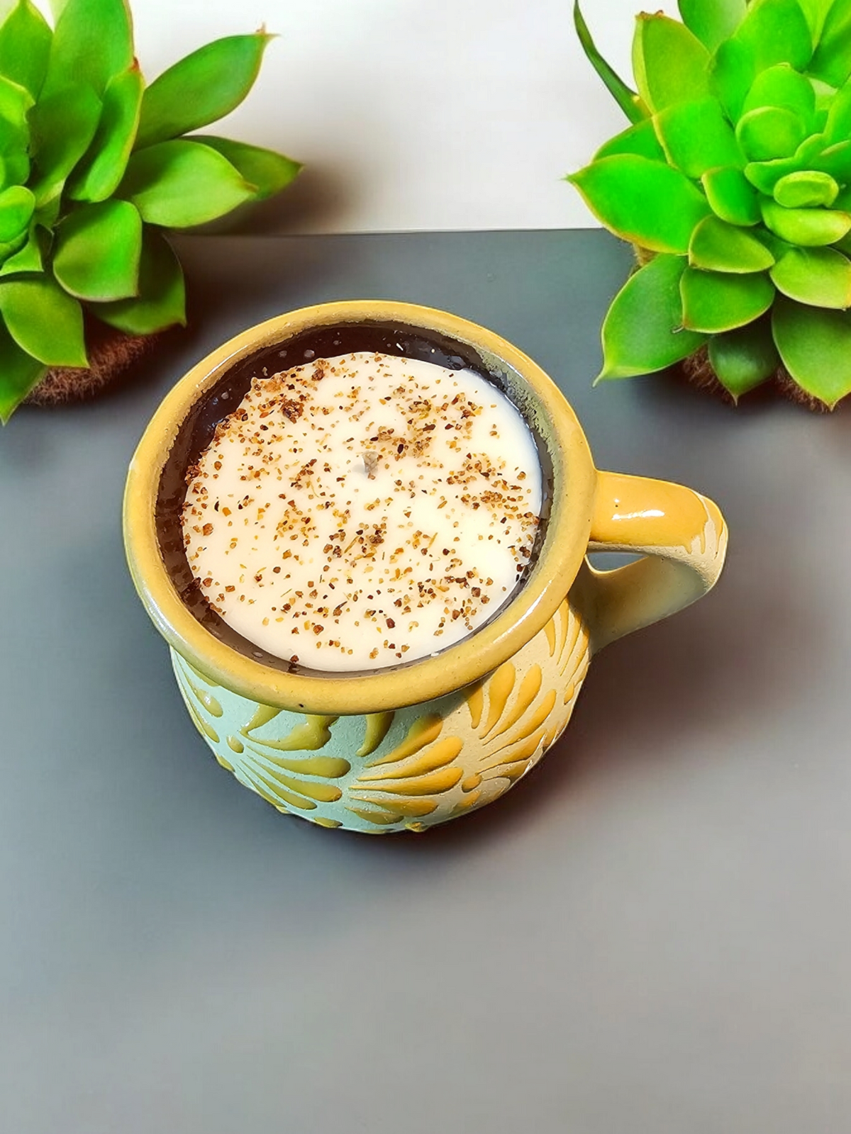 The Vela Lady Mangoneada soy wax candle in a hand-painted yellow Mexican barro mug with decorative spice topping.